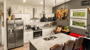 Una cocina moderna con refrigerador de acero inoxidable, dos hornos, pileta integrada y una isla grande con taburetes de bar.