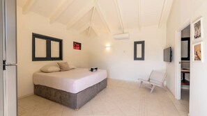 A bedroom with a bed, a chair, a TV, and a door leading to a bathroom. - Villa Kokolishi - Coral Estate Resort (Sint Willibrordus)