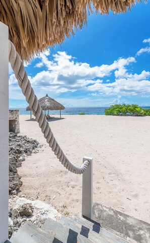 A rope tied to a concrete post on a sandy beach with a thatched-roof structure in the background. - Villa Kokolishi - Coral Estate Resort (Sint Willibrordus)
