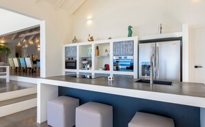 A modern kitchen with a central island, built-in appliances, and a dining area with chairs. - Villa Kokolishi - Coral Estate Resort (Sint Willibrordus)