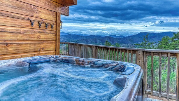 Una baita di legno con vasca idromassaggio su una terrazza con vista sulle montagne.