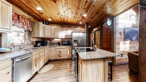 Una cucina con mobili in legno, piani di lavoro in granito, elettrodomestici in acciaio inossidabile e soffitto in legno.