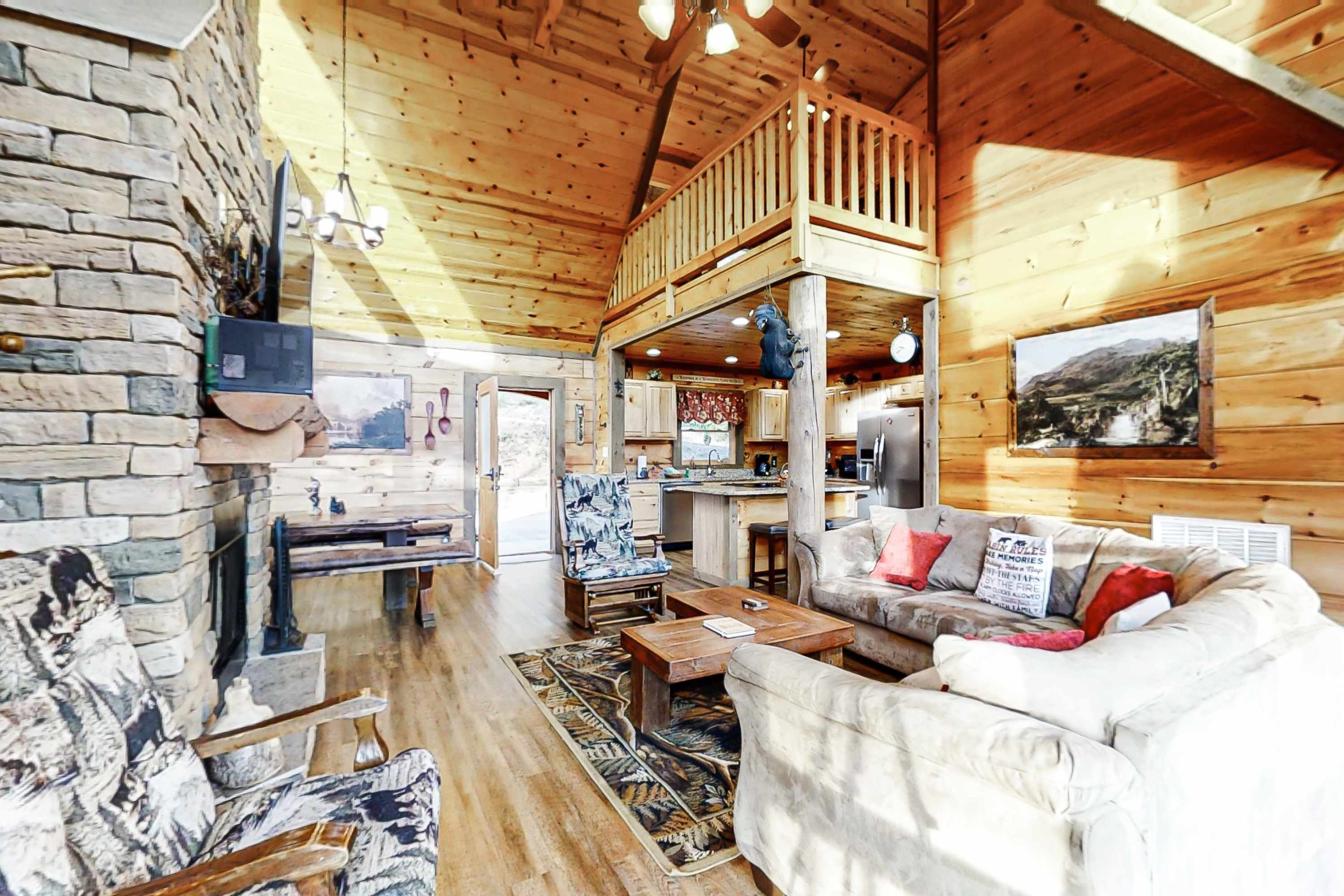 Un intérieur de chalet chaleureux avec une cheminée en pierre, des murs en bois, une chambre en mezzanine et un coin repas.