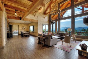 A spacious living area with wooden floors, large windows offering mountain views, and a cozy seating arrangement. - Panoramic Mountain Views, Game Room, Home Theater (Sevierville)