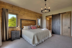 A bedroom with a large bed, wooden walls, a chandelier, and a sliding barn-style door. - Panoramic Mountain Views, Game Room, Home Theater (Sevierville)