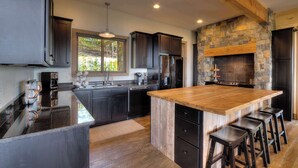 A modern kitchen with dark cabinetry, a large island with stools, and a stone fireplace. - Cozy Cabin W Home Theater, Sleeps 15, Hot Tub, Views (Sevierville)