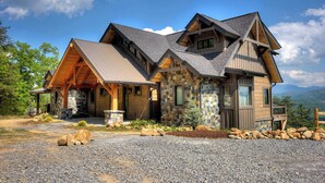 A large, multi-story log cabin with a stone foundation and a sloped roof. - Cozy Cabin W Home Theater, Sleeps 15, Hot Tub, Views (Sevierville)