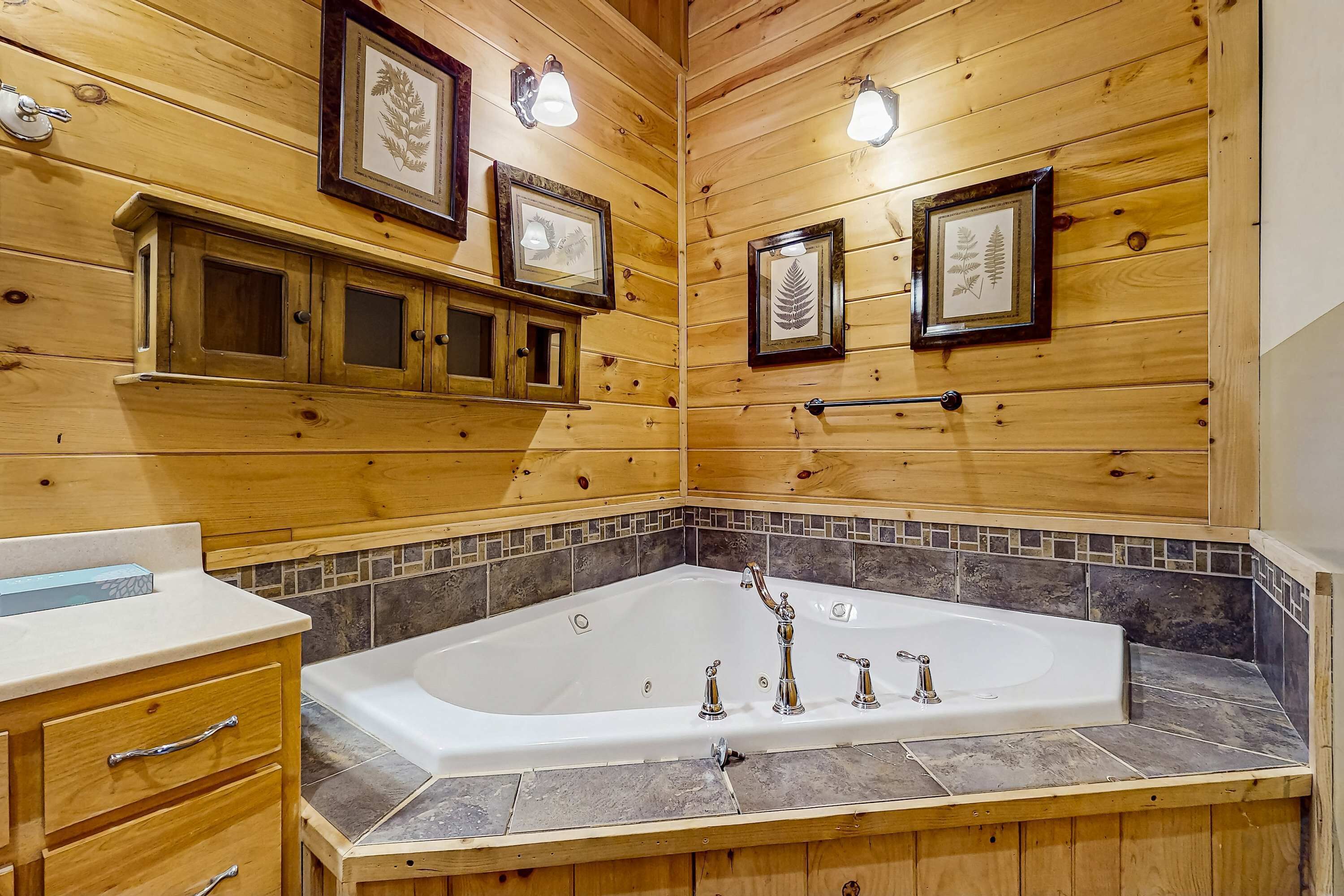 A wooden cabin bathroom with a large bathtub, wooden cabinets, and framed botanical prints on the walls.
