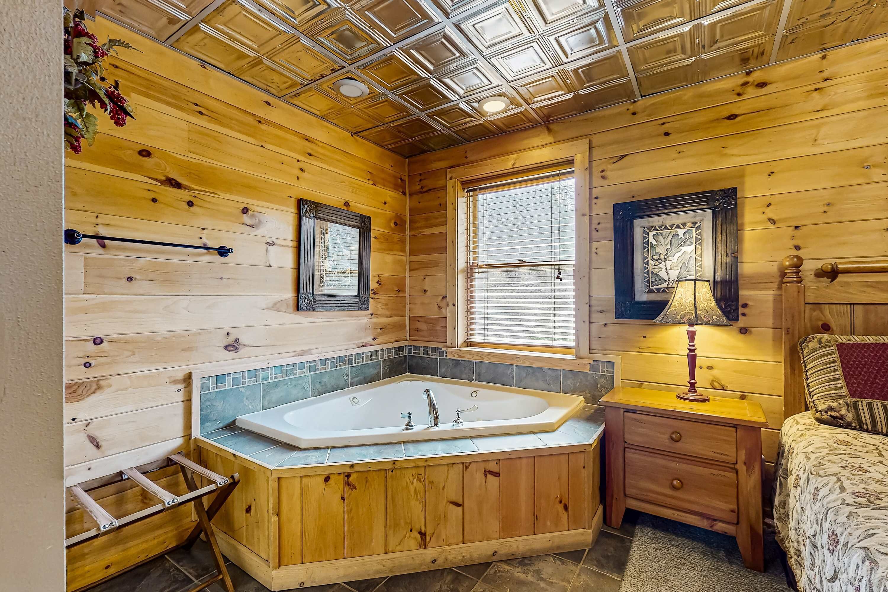 Ein Badezimmer einer Holzhütte mit Badewanne, Waschtisch mit Spiegel und Fenster mit Jalousien.