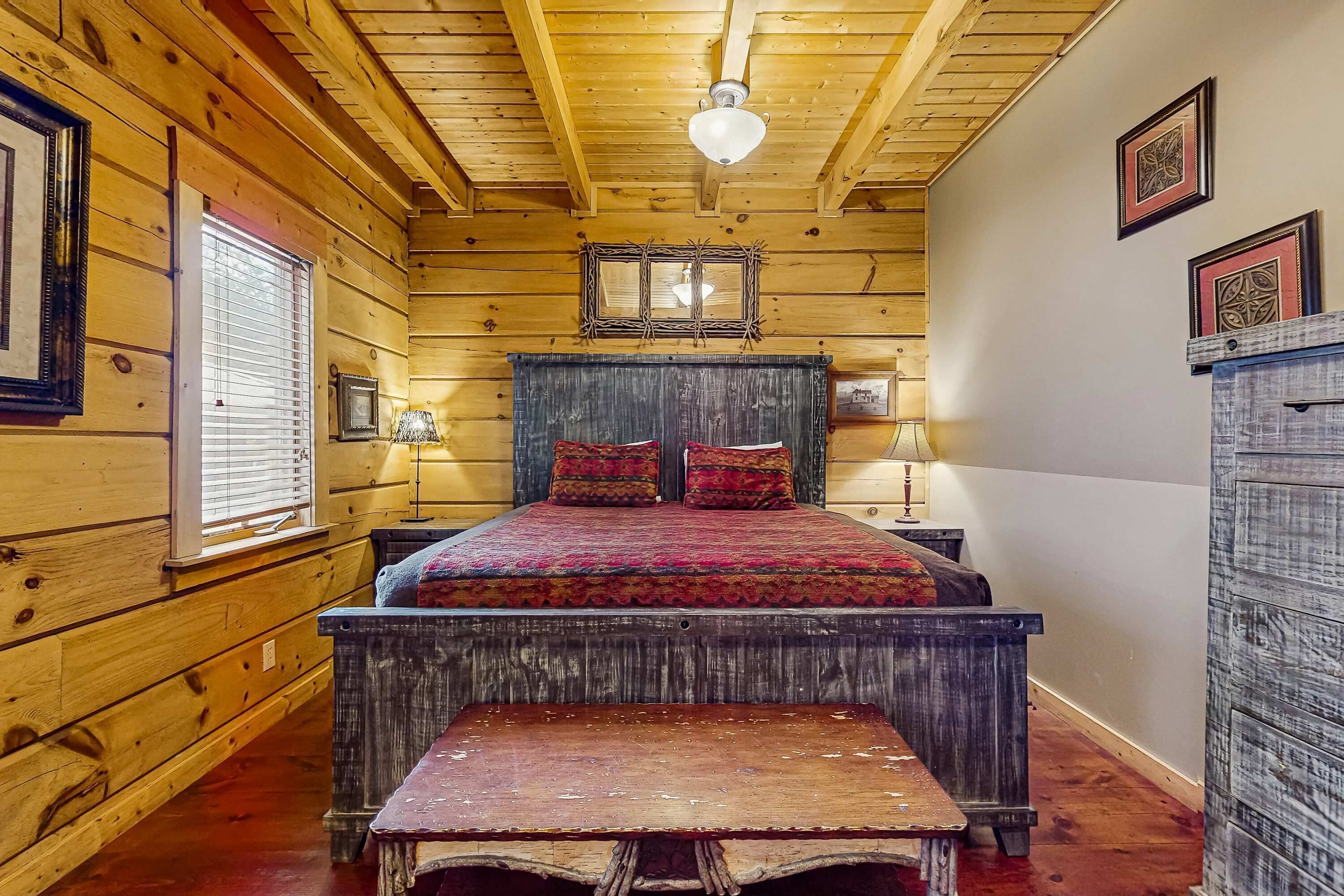 Un dormitorio de estilo cabaña de troncos con una cama de madera, un banco y un techo rústico.