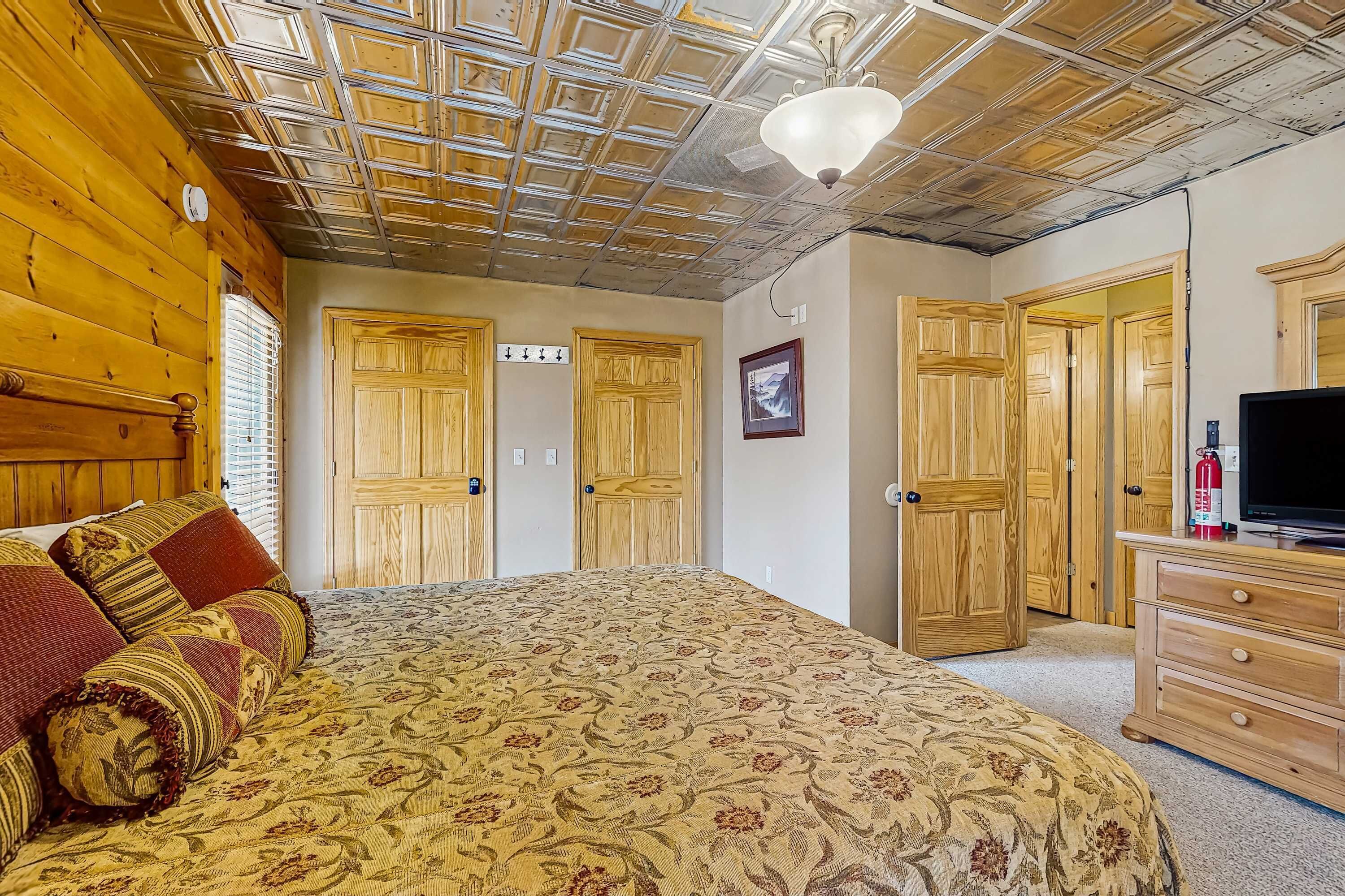 A bedroom with a wooden ceiling, a bed with floral bedding, wooden wardrobes, and a television on a dresser.
