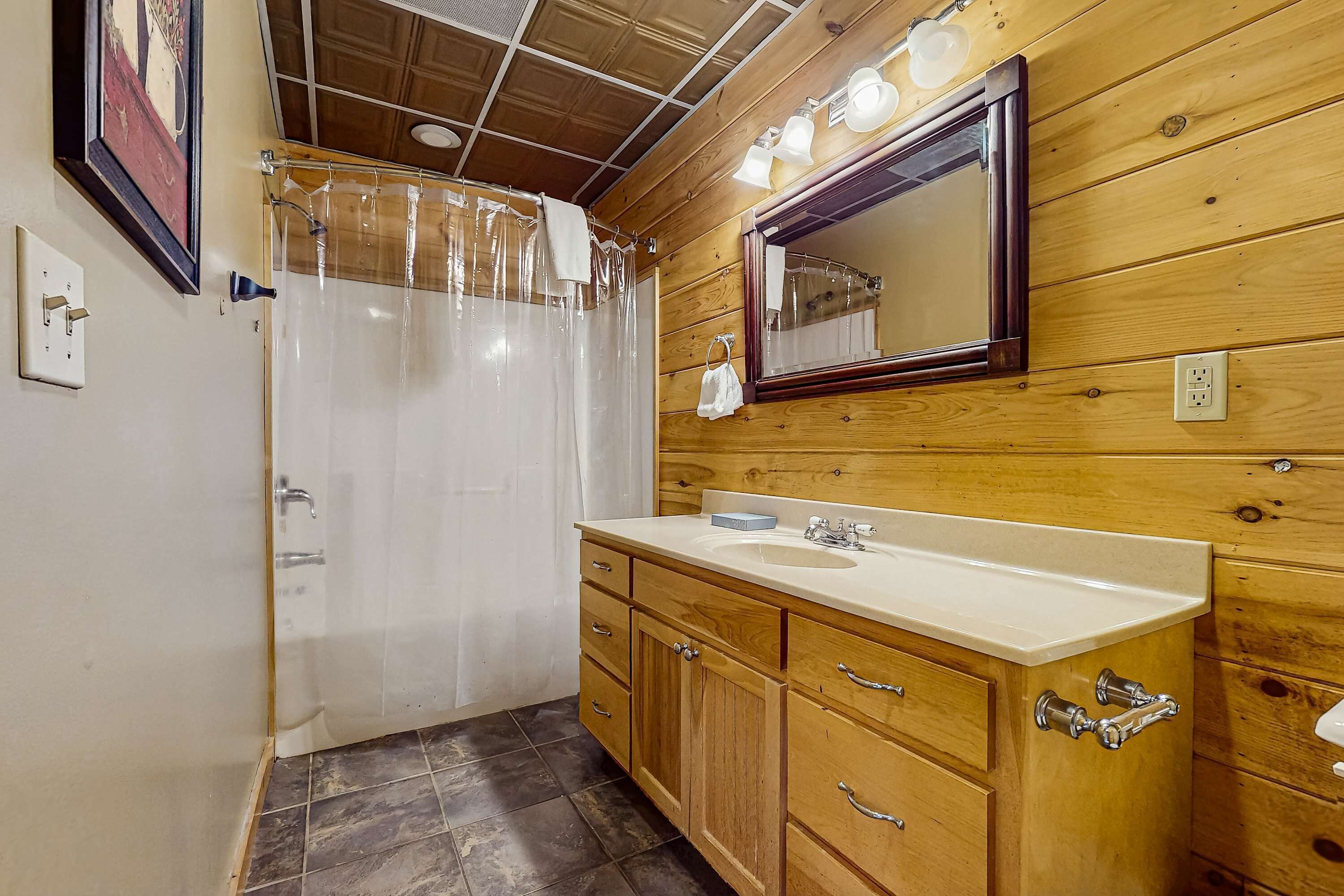 Een badkamer met houten lambrisering, een douche, een wastafel en een spiegel.