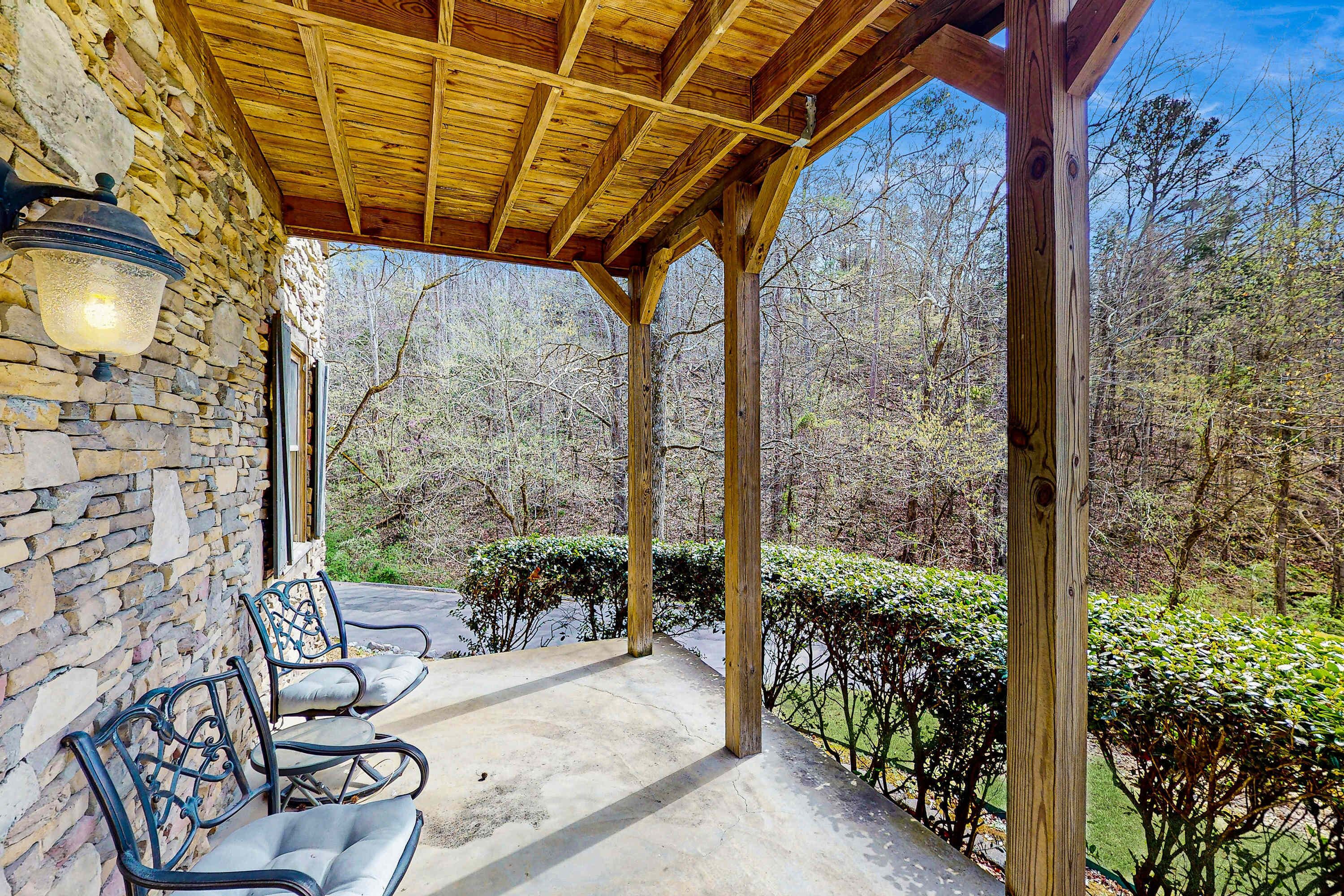 Eine überdachte Terrasse mit Steinmauern und Holzbalken, mit zwei Metallstühlen und einer an der Wand befestigten Leuchte.