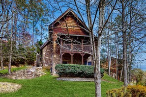 Eine Blockhütte mit Steinuntergrund, Holzbalkon und einer Steintreppe, die zum Eingang führt.
