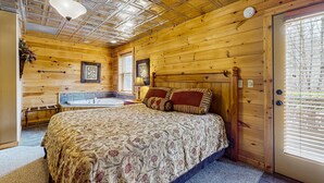 Quarto de cabana de madeira com cama, banheira embutida e uma janela grande com persianas.