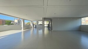 Ett tomt, rymligt inomhusområde med högt tak och stora fönster, med ett klinkergolv och en minimalistisk design.