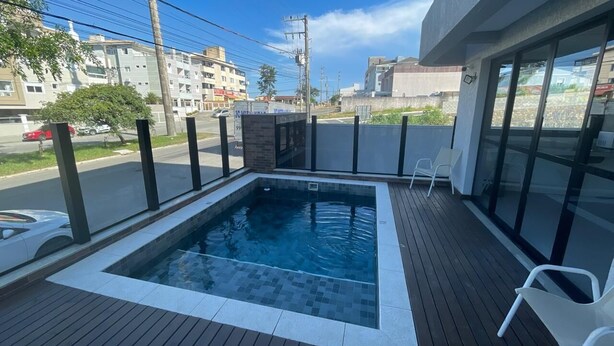 En swimmingpool med ett kaklat poolområde, omgiven av en låg mur och glasdörrar, med utsikt över gatan och byggnaderna i bakgrunden.