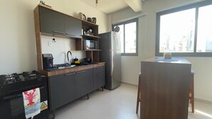 Ett kompakt kök med en gasspis, mikrovågsugn och kylskåp. Det finns en liten matplats med ett bord och stolar.