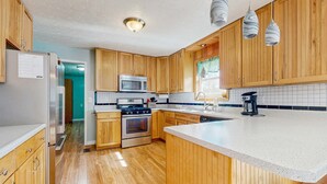 Una cocina con armarios de madera, un refrigerador de acero inoxidable, un microondas, un horno y una cafetera.