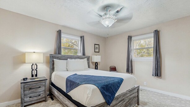 Un dormitorio con cama, mesita de noche, lámpara y ventilador de techo.