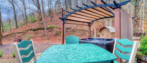 An outdoor patio with a table and chairs, a hot tub, and a wooden structure.