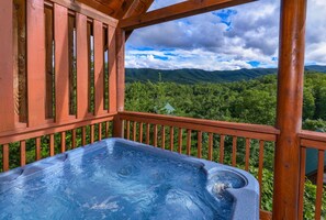 Een hottub op een houten terras met uitzicht op een bebost berglandschap.