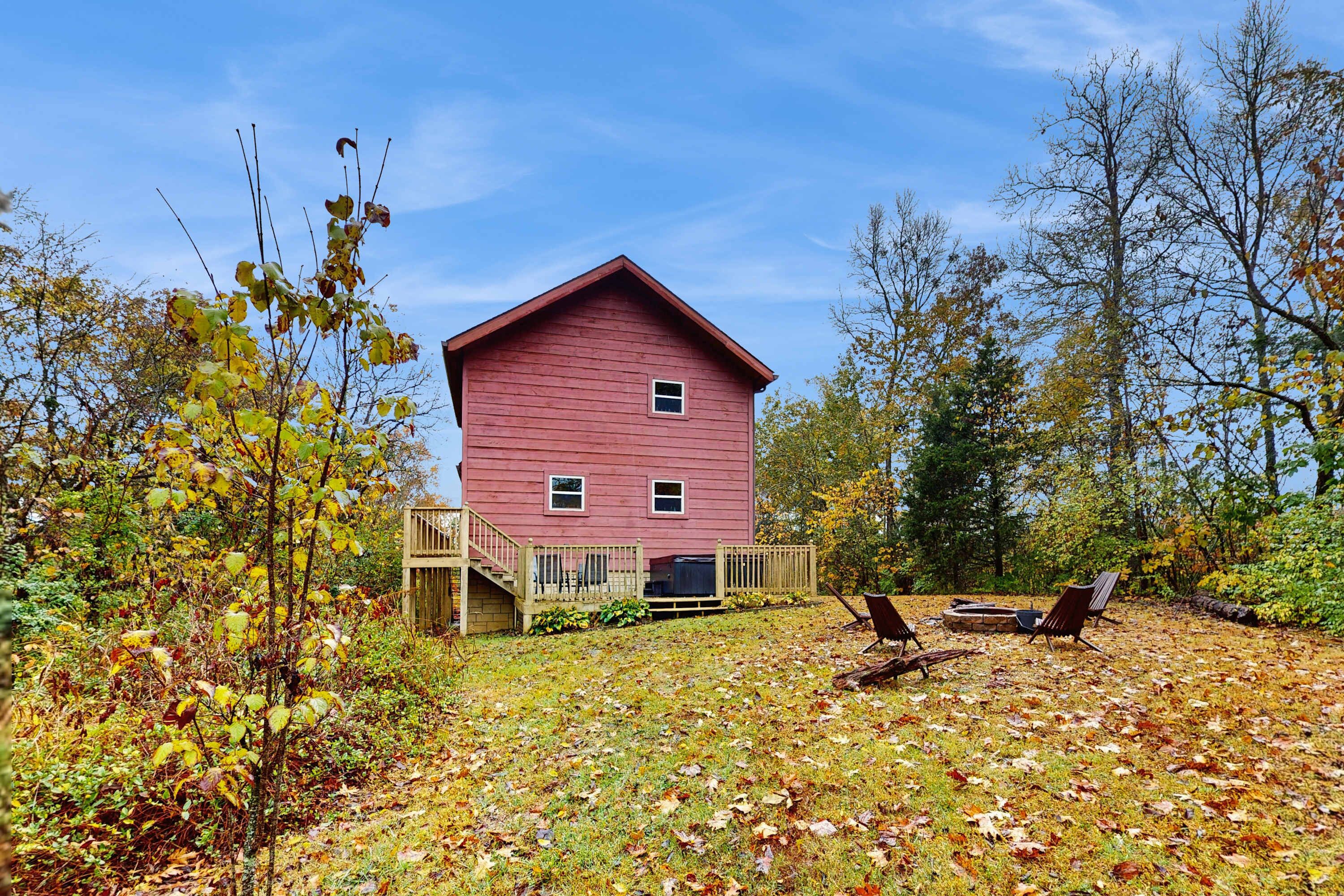 Een rode houten woning met terras, omringd door bomen en herfstbladeren.
