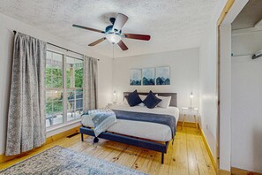 A bedroom with a bed, a ceiling fan, a nightstand, a window with curtains, and a view of greenery outside. - Serene Cabin, Sleeps 8, Hot Tub, Fire Pit, Game Room (Sevierville)