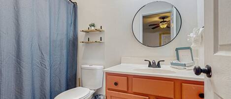 Un baño con inodoro, lavamanos, espejo y cortina de ducha.