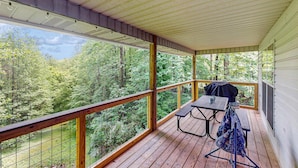 Une terrasse extérieure couverte, dotée d’une table de pique-nique et de chaises, qui offre une vue sur une zone boisée.