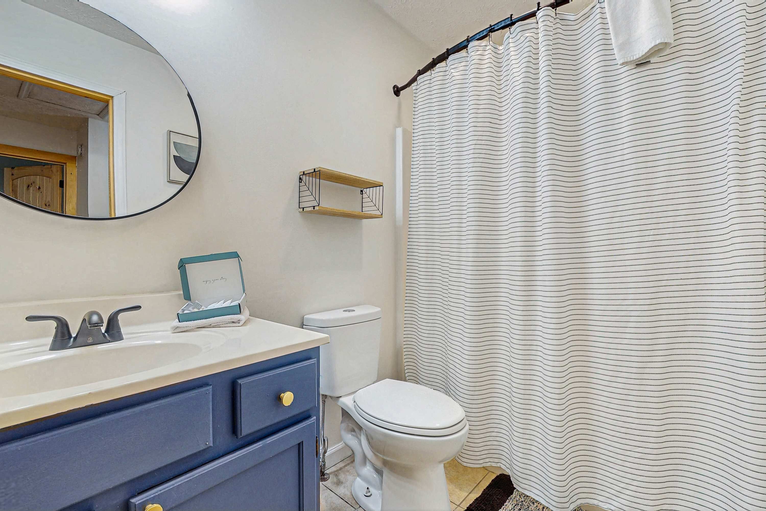 A bathroom with a white toilet, a blue cabinet, a white sink, a mirror, and a striped shower curtain.