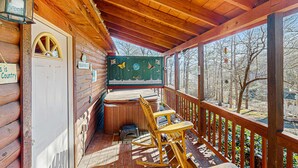 Eine Holzterrasse mit einem Schaukelstuhl, einem Whirlpool und Blick auf einen Fluss und Bäume.