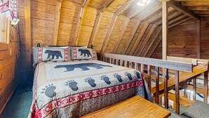 Eine Holzhütte mit hohen Decken, einem Bett mit einer Bettdecke mit Bärenmotiv und einer hölzernen Bank.