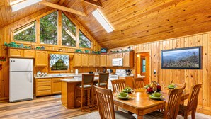 A wooden cabin interior with a kitchen, dining area, and large windows. - Always Delightful - Sleeps 10, Hot Tub, Fire pit, Games (Sevierville)