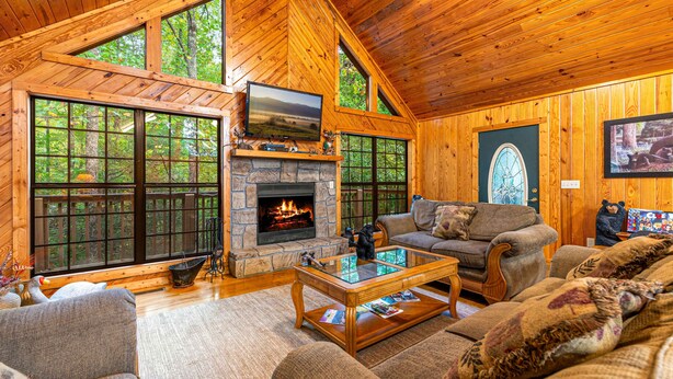 A cozy log cabin interior with a stone fireplace, large windows, and a comfortable seating area. - Always Delightful - Sleeps 10, Hot Tub, Fire pit, Games (Sevierville)