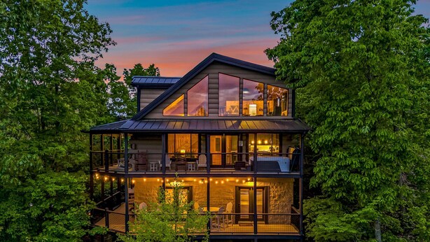 A multi-story modern house with a balcony and outdoor seating area, surrounded by dense trees. - The Treehouse, Sleep 12・Hot Tub・Firepit・Game Room (Sevierville)