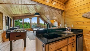 A cozy wooden interior with a foosball table, a kitchen island, and a dining area with a view of the outdoors. - The Treehouse, Sleep 12・Hot Tub・Firepit・Game Room (Sevierville)