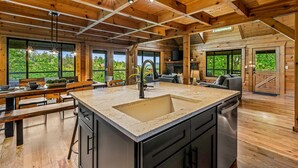 A spacious kitchen with a large island, wooden ceiling beams, and large windows offering views of the outdoors. - The Treehouse, Sleep 12・Hot Tub・Firepit・Game Room (Sevierville)