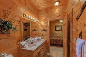 A wooden cabin bathroom with a double sink vanity, a mirror with lights, a toilet, and a door with a bear decoration. - Pet Friendly Near Dollywood Cabin・Hot tub・Views (Sevierville)