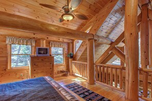 A log cabin room with a bed, dresser, TV, and windows overlooking a forest. - Pet Friendly Near Dollywood Cabin・Hot tub・Views (Sevierville)