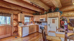 A log cabin with wooden floors, a kitchen with a microwave, stove, and refrigerator, and a dining area with a table and chairs. - Pet Friendly Near Dollywood Cabin・Hot tub・Views (Sevierville)