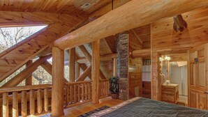 A log cabin bedroom with a large bed, wooden beams, a stone fireplace, and a balcony with a railing. - Pet Friendly Near Dollywood Cabin・Hot tub・Views (Sevierville)