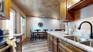 A kitchen with wooden cabinets, a granite countertop, a stainless steel sink, and a clock on the wall. - 2 Mi to DT PIgeon Forge・Serene Stay・Hot Tub・Grill (Pigeon Forge)