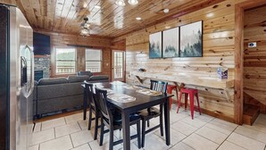 Interior de uma cabana de madeira com uma mesa de jantar, cadeiras, um sofá e uma lareira.