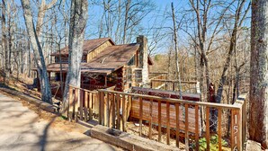 Un chalet rustique doté d’une terrasse en bois et d’une cheminée, entouré d’arbres.