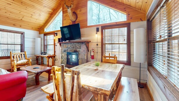 L’intérieur chaleureux d’un chalet avec une cheminée en pierre, une table à manger en bois et une tête de cerf accrochée au mur.