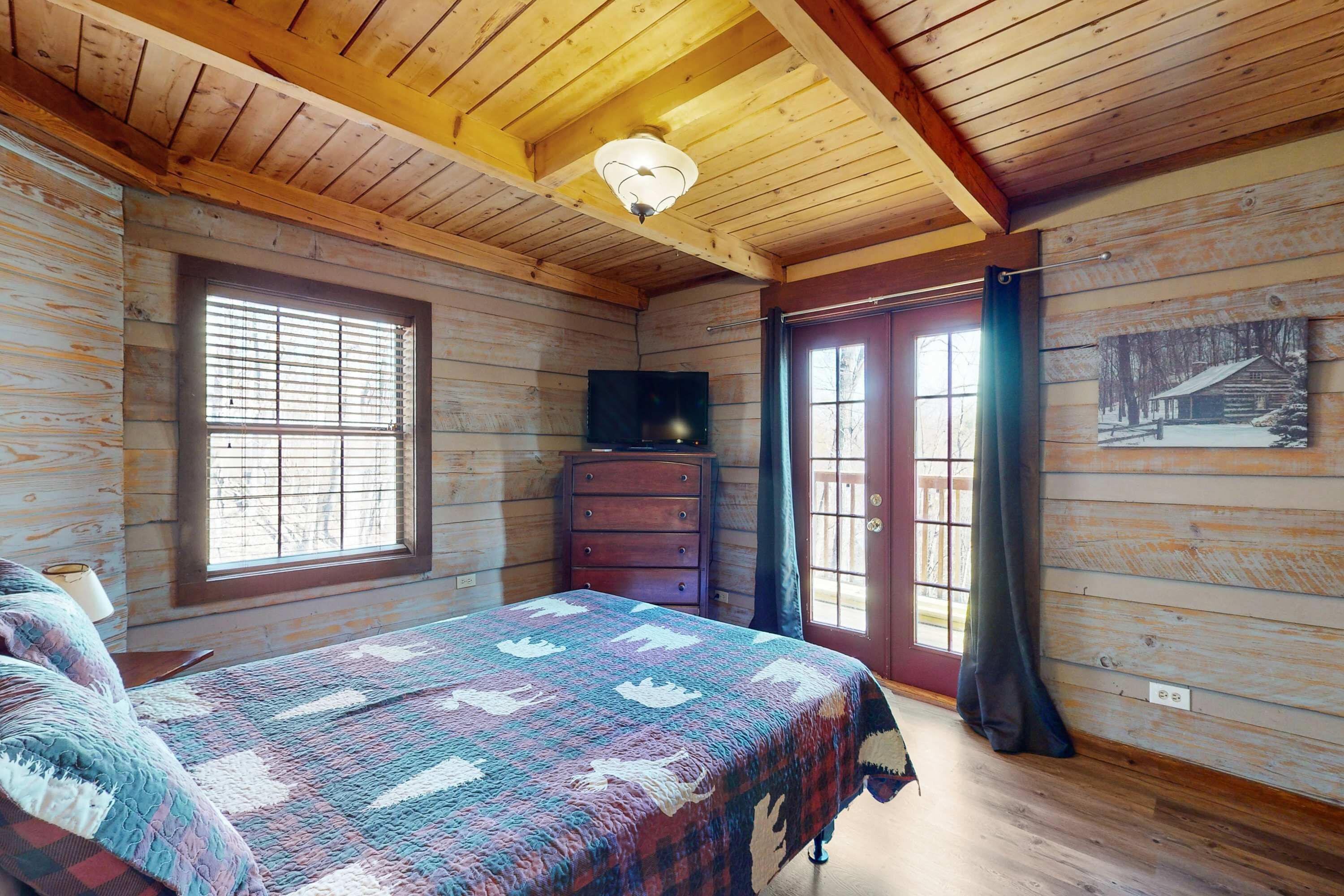 A wooden cabin bedroom with a bed, dresser, and a television.