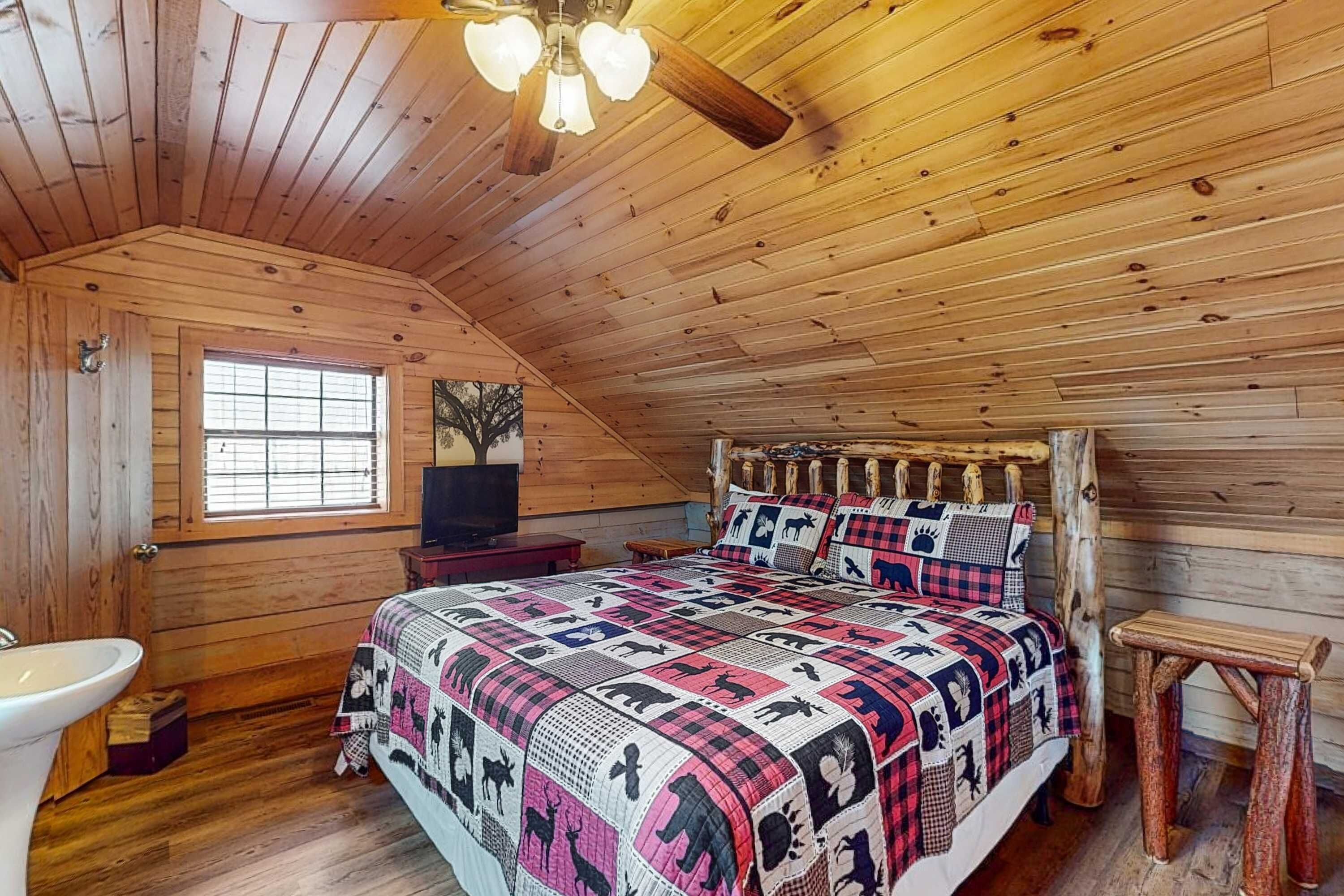 A wooden cabin bedroom with a bed, a window, a sink, and a ceiling fan.