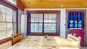 Une table à manger en bois, ornée d’une plante au centre, entourée de chaises en bois, dans une pièce aux murs en bois et à la porte rouge.