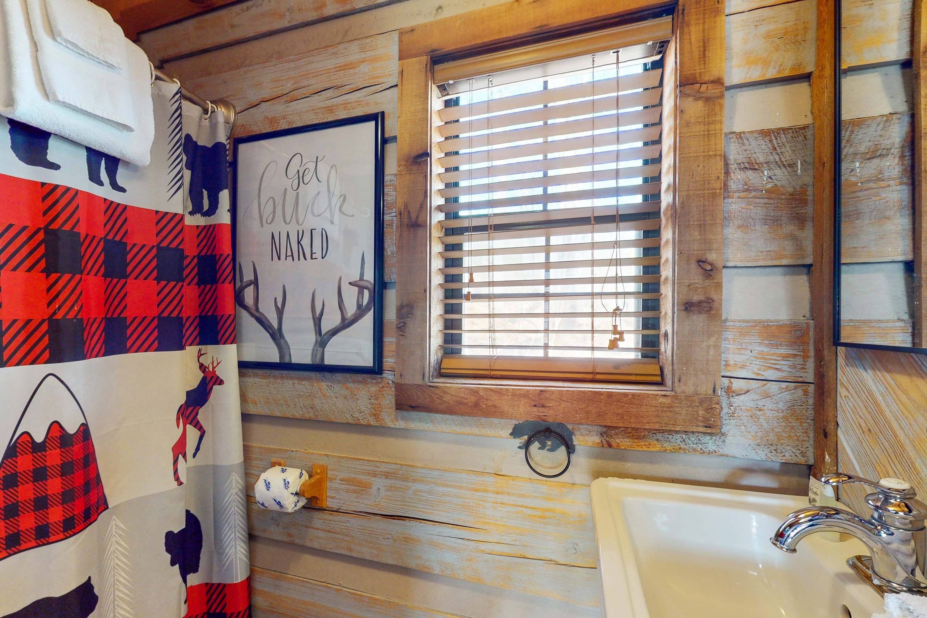 Un baño rústico con paredes de madera, una ventana con persianas, un lavabo y un perchero para toallas.